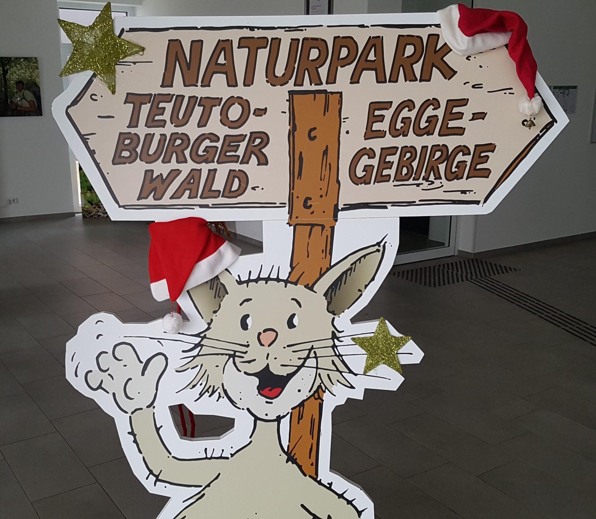 Pappaufsteller der gezeichneten Wildkatze "Teutus" winkend am Aufsteller Naturpark Teutoburgerwald/ Eggegebirge